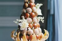 a small and whimsical croquembouche with caramelized and cied pieces, white blooms and a creative stand