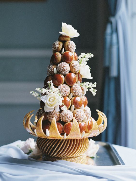 a small and whimsical croquembouche with caramelized and cied pieces, white blooms and a creative stand