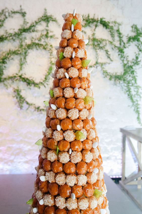 a tall and refined croquembouche with icing, caramel, sugar greenery and white buds for a spring wedding