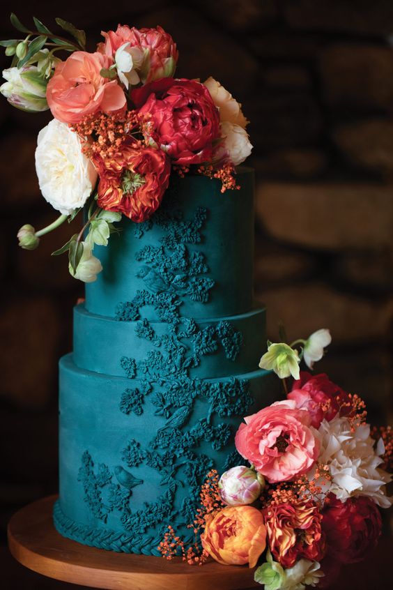 a teal wedding cake with a whimsical pattern, with white, coral and orange blooms and greenery for a wedding with much color