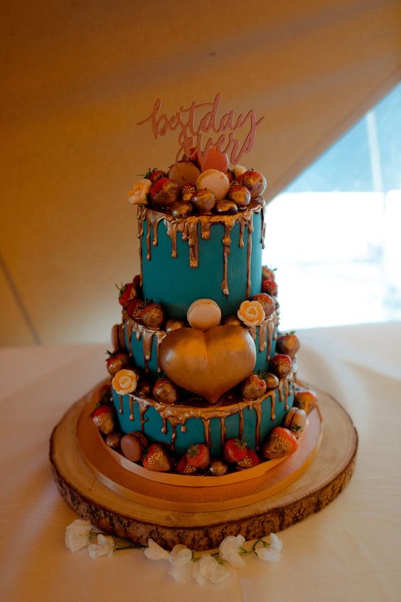 a teal wedding cake with copper drip, fresh berries in copper drip, a large copper heart and a calligraphy topper