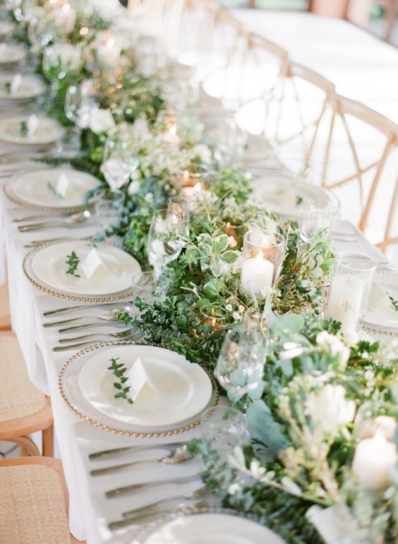 a beautiful textural greenery table garland with various types of greenery and succulents plus candles in glasses is a cool idea