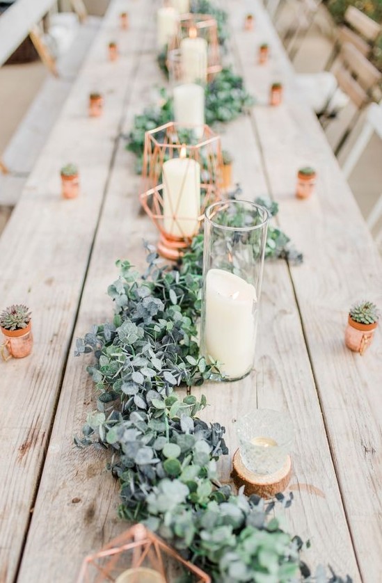 a cute greenery and foliage table runner with candles and copper canlde holders is a chic idea