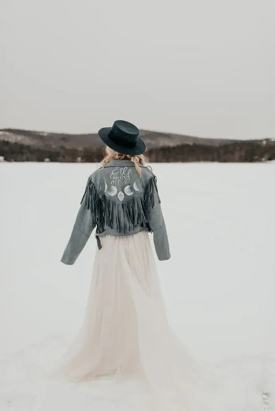 a blue denim bridal jacket with long fringe, calligraphy and celestial painting plus a navy hat for a winter boho bride