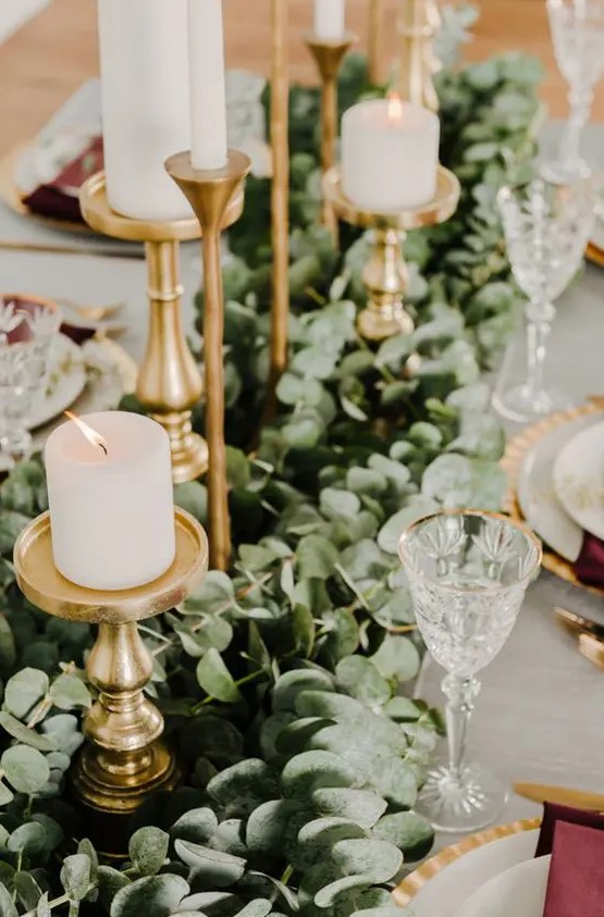 a lush eucalyptus table runner with gold candle holders and pillar candles for a timelessly elegant look