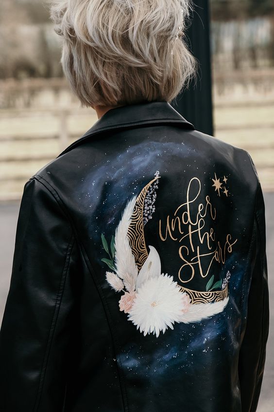 a black leather jacket with a night sky, a large half moon, blooms and gold calligraphy is a catchy and lovely idea