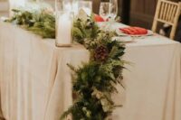 20 an evergreen and greenery table runner with pinecones and pillar candles is a classic decor idea for a winter wedding