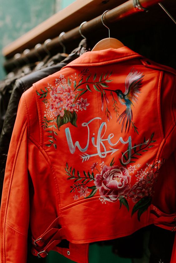 an orange cropped leather bridal jacket with bold painted blooms, a humming bird and calligraphy is a super bold and catchy idea