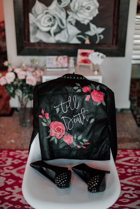 a black leather jacket with painted bright blooms and greenery, white calligraphy and studs plus studded shoes for an edgy bride