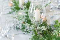 29 a delicate greenery and white flower wedding table garland with some pillar candles is a stylish decor idea for a spring wedding