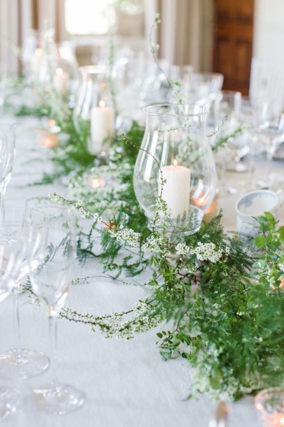 a delicate greenery and white flower wedding table garland with some pillar candles is a stylish decor idea for a spring wedding