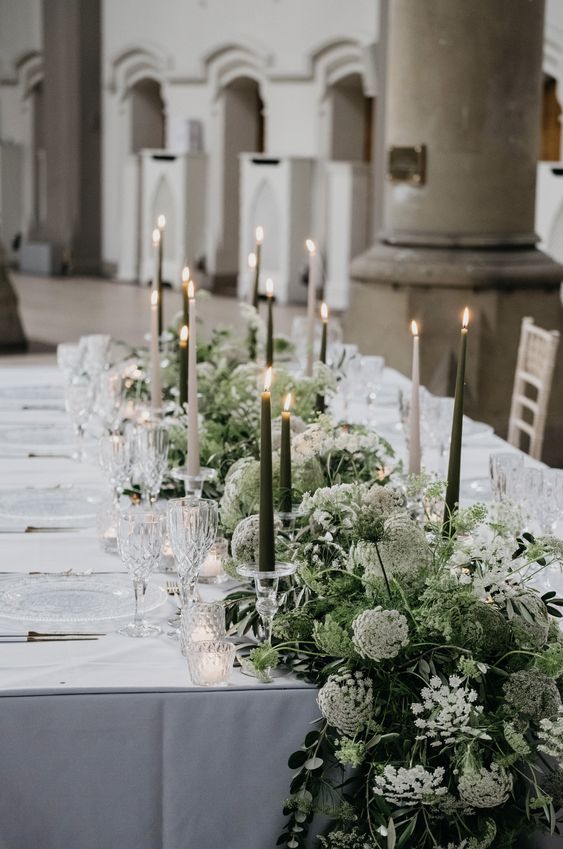 a lush and beautiful greenery table runner with white blooms and black and white candles is a chic idea for a spring or summer celebration