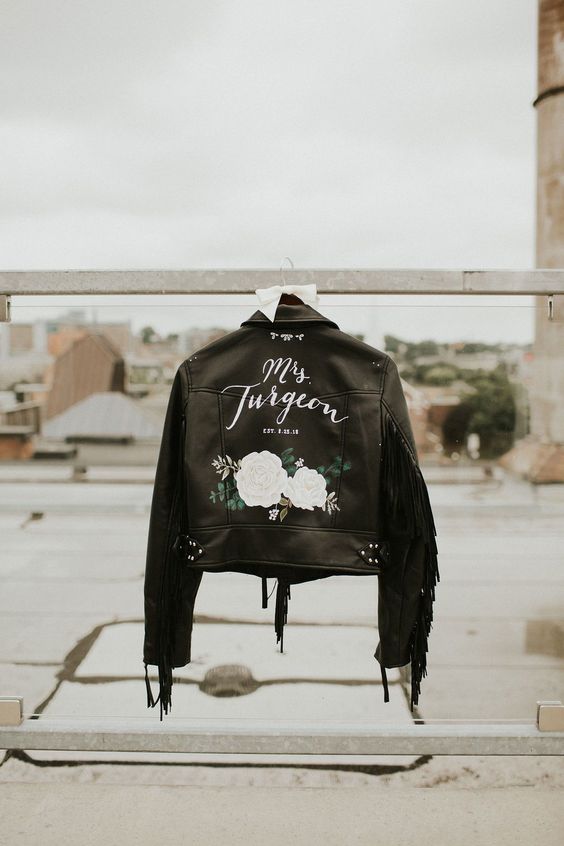 a black leather jacket with painted white blooms, white calligraphy and fringe on the sleeves is a stylish idea