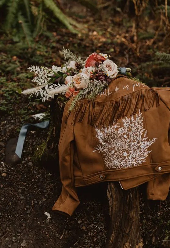 a brown suede jacket with hand painted white blooms, calligraphy and long fringe on the back is ideal for a boho bride