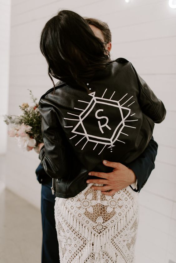 a black leather jacket with white painting and monograms is a stylish idea for a boho bride, it looks laconic and stylish