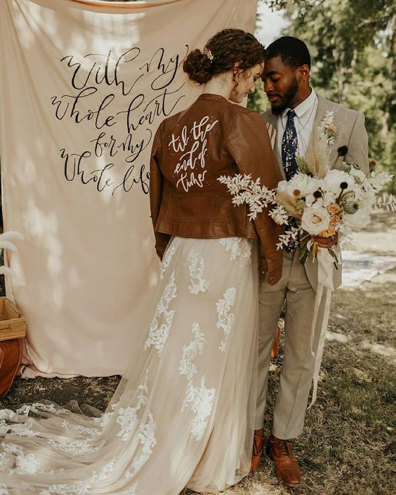 a brown leather jacket wiht white calligraphy painted is a cool and lovely cover up to rock at a boho wedding