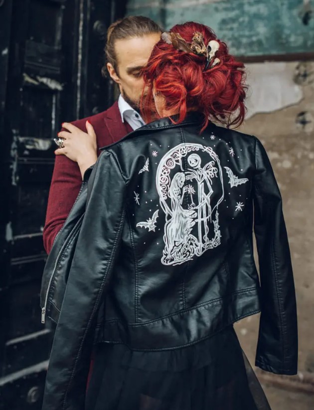 a bride wearing a black wedding dress and a black leather jacket with Tim Burton movie characters painted to personalize it