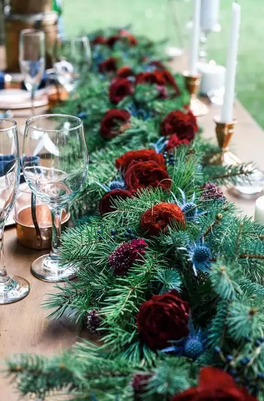 an evergreen table runner with bold burgundy blooms and thistles for a rustic winter wedding