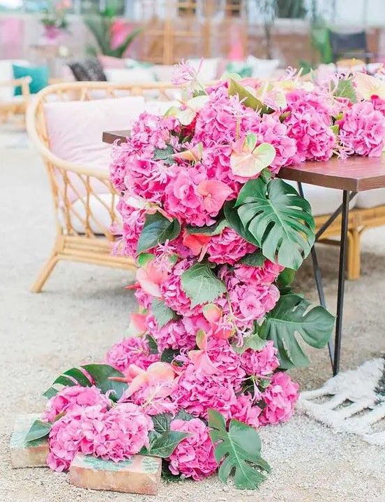 bring paradise to your wedding with a pink floral table runner of palm leaves and tropical blooms cascading down