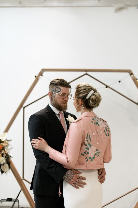 a pink cropped leather bridal jacket with painted blooms and greenery and white calligraphy is a stylish idea for a wedding