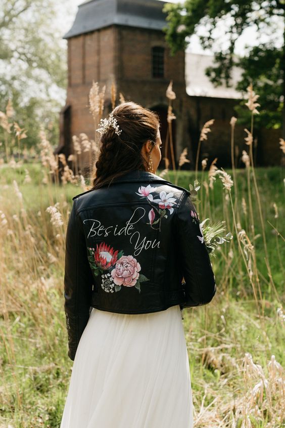 a custom black leather jacket with white calligraphy and bright painted blooms is a stylish idea for a bride