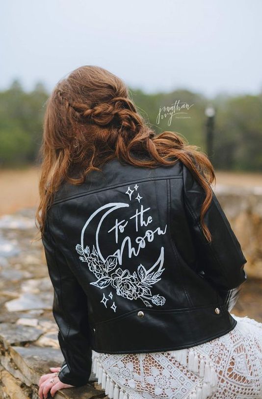 a classy black leather jacket with white calligraphy and a painted moon with blooms is a catchy idea for a celestial bride