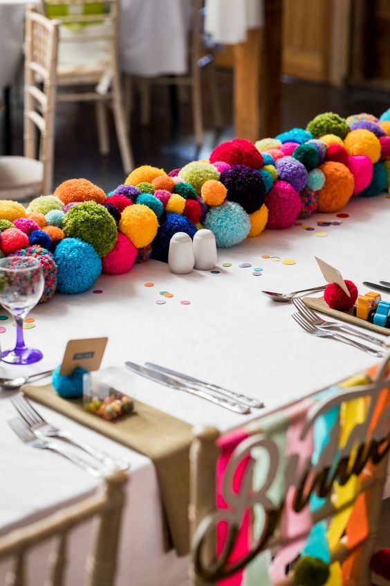 a colorful pompom table garland is a fun and cool idea for a bright wedding, and you can DIY one