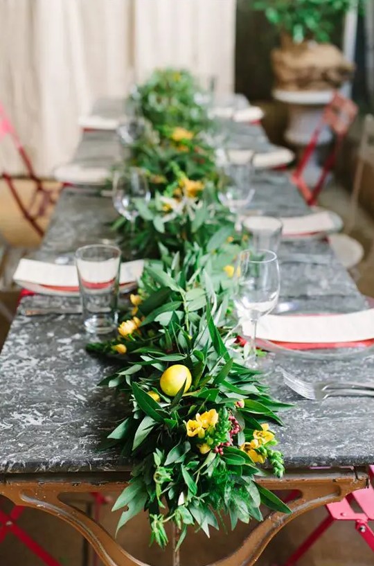 a lush and textural greenery table runner with fruits and yellow flowers incorporated for a bold look