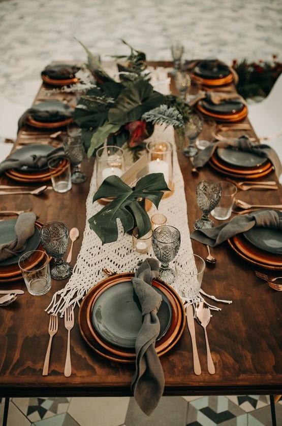a macrame wedding table runner and centerpieces of tropical leaves for a boho tropical wedding