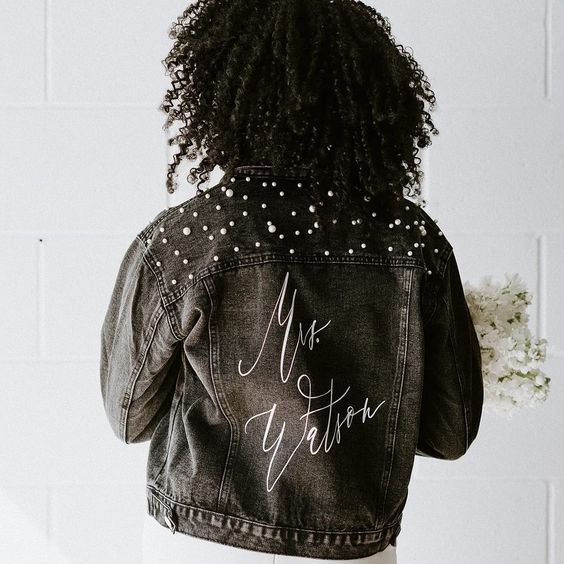 a black denim bridal jacket with white calligraphy and pearls on the shoulders is a very cool and bold solution