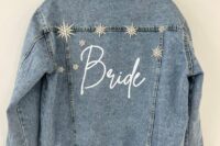 a blue denim bridal jacket with white calligraphy and large vintage star brooches that embellish the back