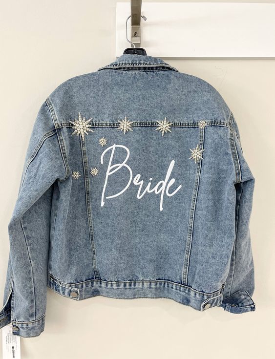 a blue denim bridal jacket with white calligraphy and large vintage star brooches that embellish the back