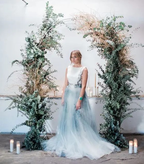 a beautiful and trendy modern wedding arch covered with lots of eucalyptus and with dried grasses is a chic idea