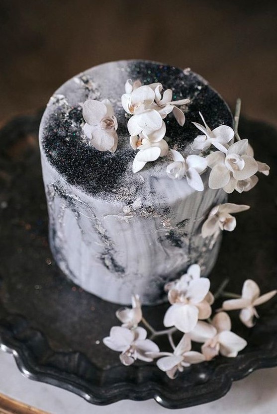 a beautiful black and white wedding cake with watercolors, silver glitter and white blooms on top looks ethereal