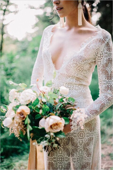 a boho lace wedding dress with a plunging neckline and long sleeves, statement earrings and a lovely neutral wedding bouquet for a summer wedding