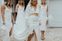 06 a bride wearing a neutral twisted crop top with puff sleeves and a maxi skirt with a slit, gold mules and a veil, bridesmaids rocking midi white dresses with slits and dusty pink mules