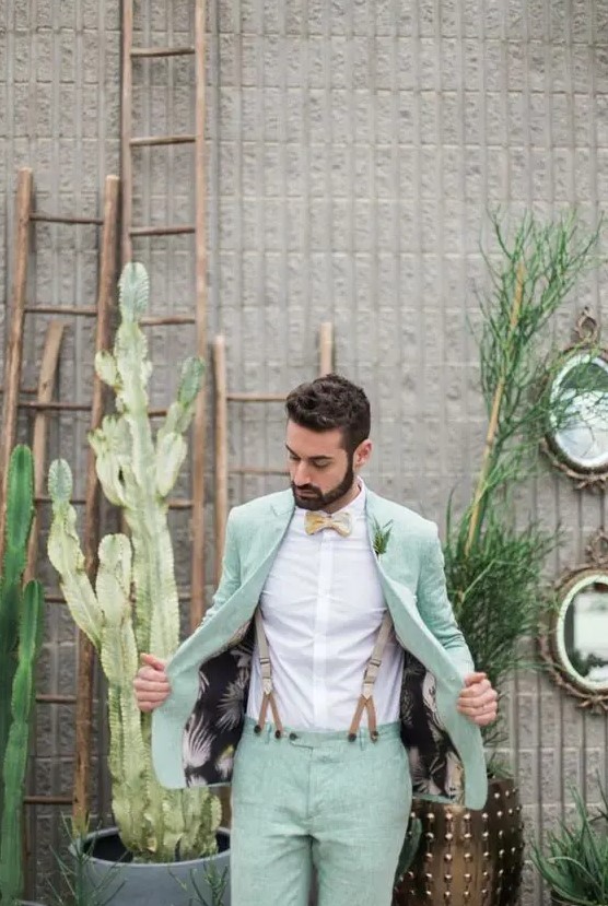 a pastel green groom's suit, a white shirt, a neutral bow tie, tan suspenders for an ultimate spring groom's look