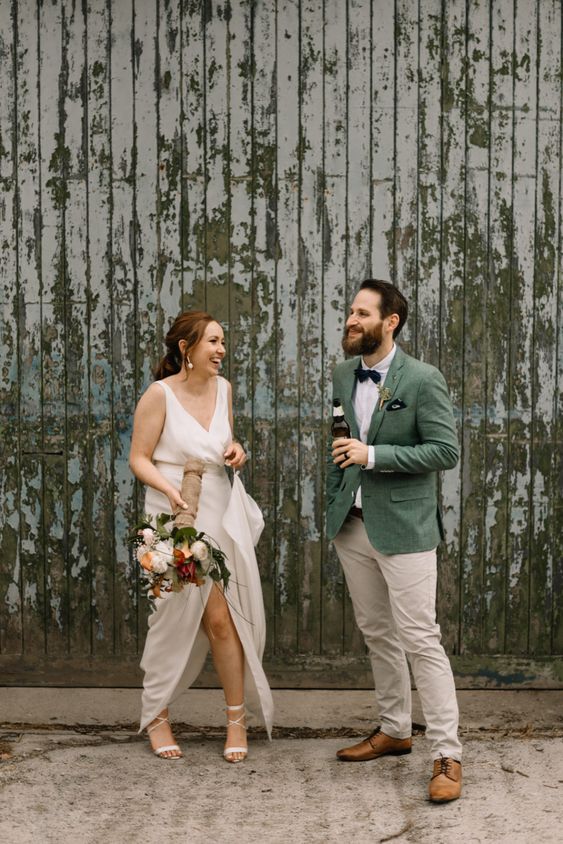 a cool boho groom's outfit with a white shirt, neutral pants, a green blazer, a black bow tie and handkerchief is relaxed and nice