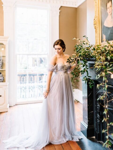 a delicate and refined lilac off the shoulder wedding dress with a lace embellished bodice and a train for a spring or summer bride