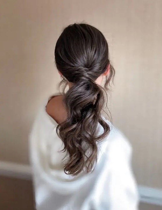 a dreamy wavy low ponytail with twisted hair and a sleek top plus locks framing the face is a lovely idea for a modern bride