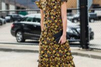 09 a bold and chic fall wedding guest look with a yellow, black and navy floral midi dress with a high neckline, ruffle cap sleeves, brown boots and a black clutch