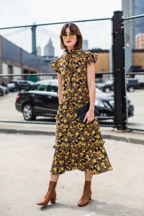 a bold and chic fall wedding guest look with a yellow, black and navy floral midi dress with a high neckline, ruffle cap sleeves, brown boots and a black clutch