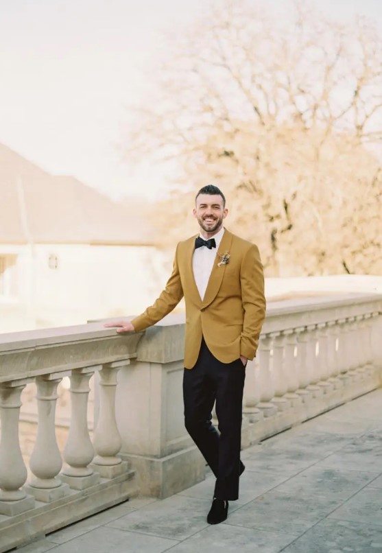 a refined groom's look with an ochre tux, black pants, loafers and a bow tie and a dried flower boutonniere