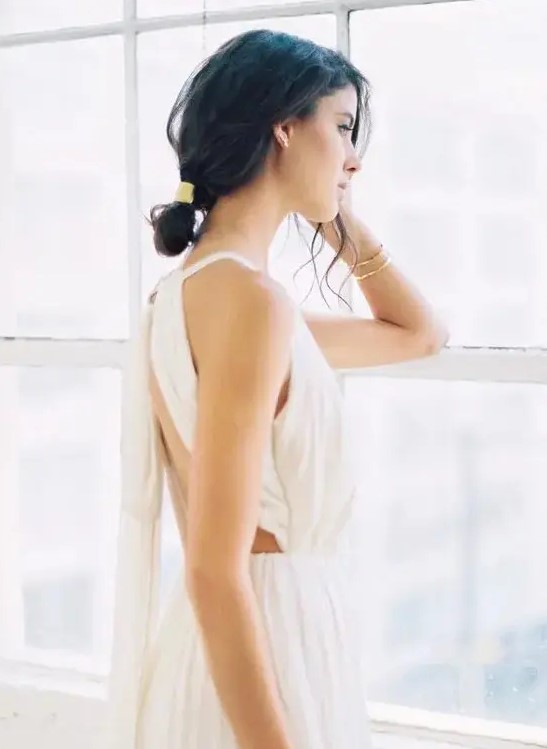 a messy low bun with bangs and a shiny accessory for a cool modern look at a destination wedding