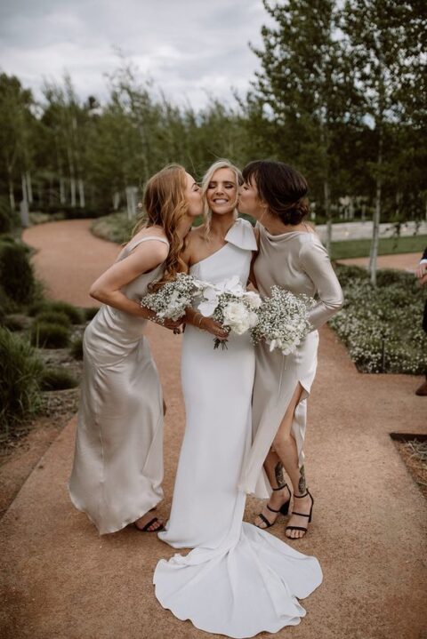 a minimalist one shoulder wedding dress with a large bow on the shoulder and a train, satin maxi bridesmaid dresses with side slits and mismatching sleeves and necklines