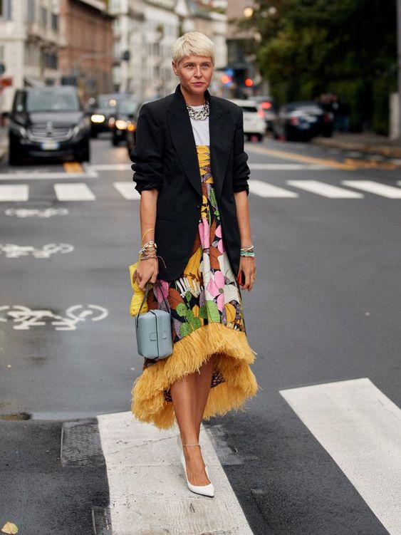 a bold midi dress with a floral print, an asymmetric skirt, yellow fringe, white shoes and an oversized black blazer, a green bag
