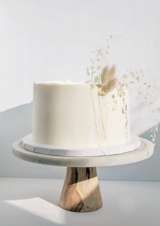 a minimalist white one-tier wedding cake decorated with dried grasses in neutral shades is a lovely solution for an organic wedding