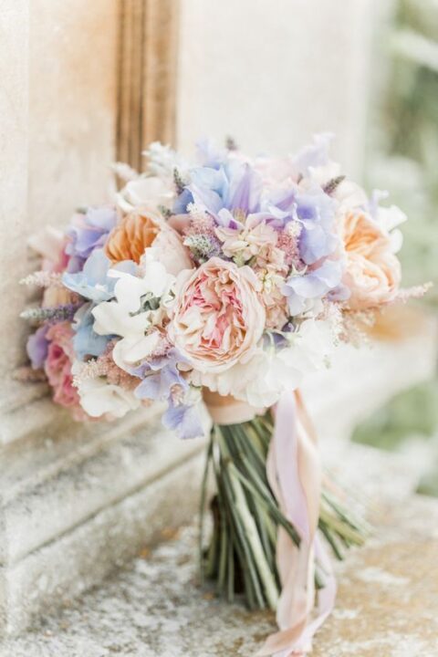 a beautiful spring wedding bouquet with lilac, blue, blush, peachy blooms, lavender and long ribbons is a stylish idea