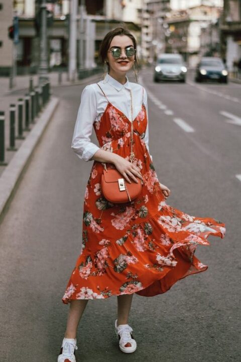 a bright and cool look with a white shirt, an orange floral print midi dress, white sneakers and an orange bag for a summer to fall wedding