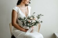 13 a modern glam bridal look with a plain fitting wedding dress with lace inserts, a deep neckline and cap sleeves plus statement pearl earrings